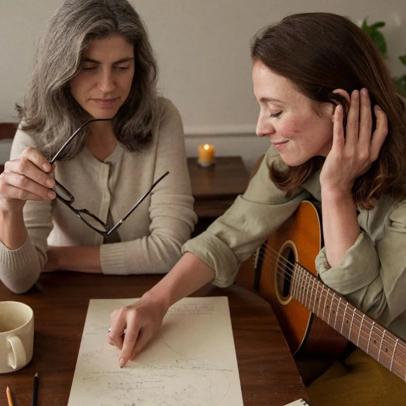 An astrologer reading a birth chart and an artist composing the AstroSong together by warm evening light
