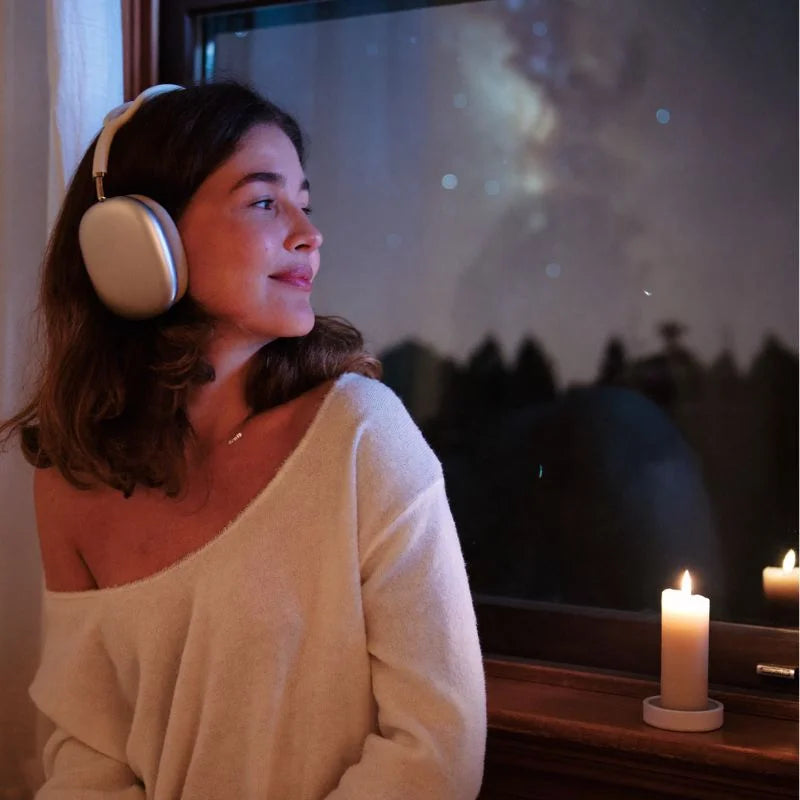 A woman by a window at night listening to her AstroSong with a candle beside her